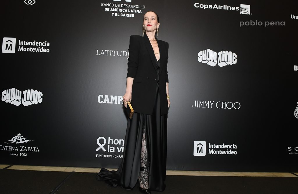 Invitada de blazer negro y falda larga posa frente al panel de sponsors en el Renato Papiccio Runway, Sofitel Montevideo