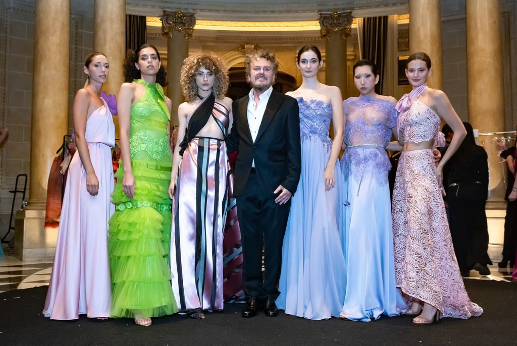 Diseñador posa junto a seis modelos con vestidos en tonos lavanda, verde, celeste y rosa en el Renato Papiccio Runway, Sofitel Montevideo