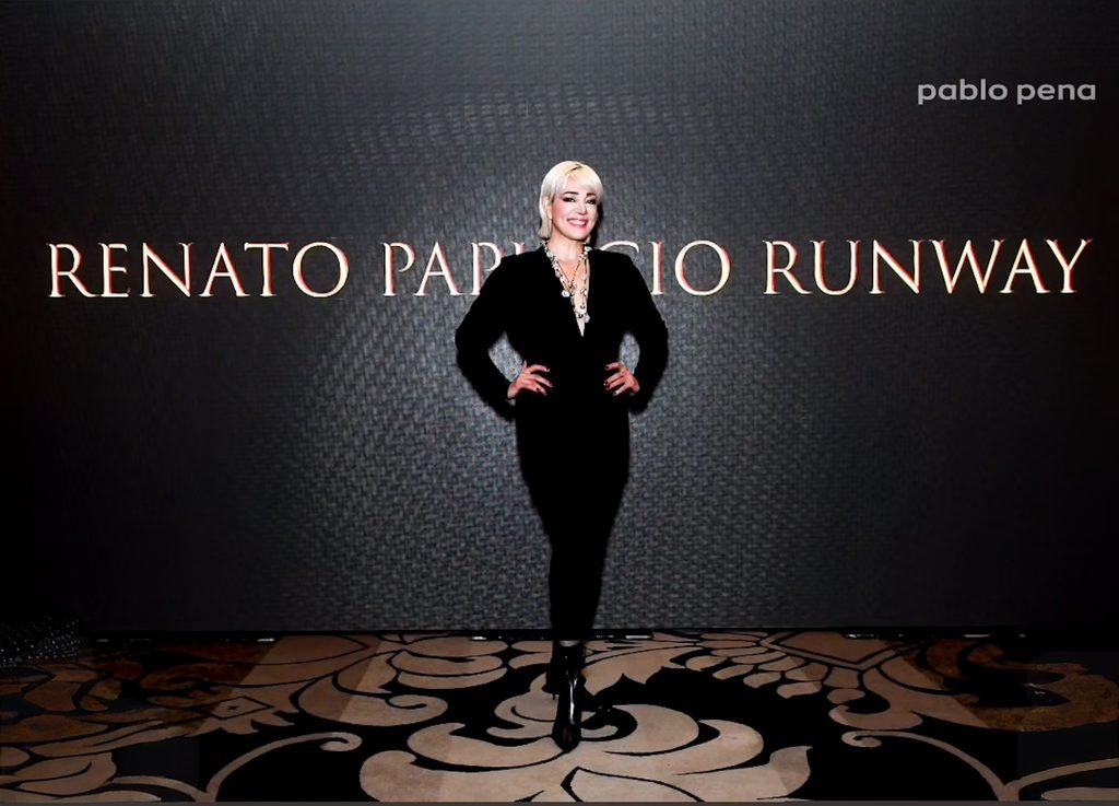 Invitada rubia con enterito negro posa frente al cartel del Renato Papiccio Runway
