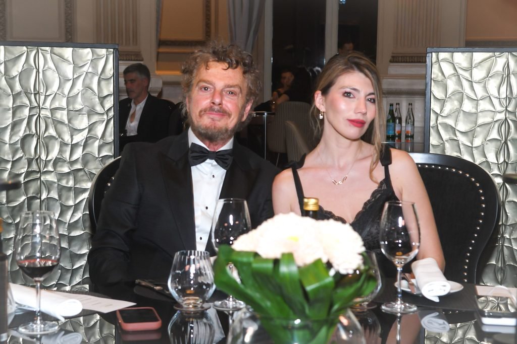 Hombre de esmoquin y mujer rubia sentados a la mesa durante la cena en el Renato Papiccio Runway, Sofitel Montevideo